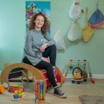 a childcare practitioner sits in a nursery surrounded by toys
